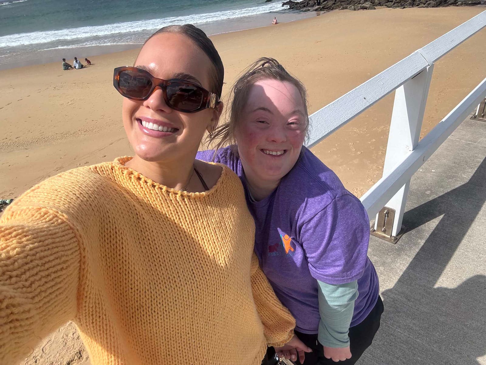 A Pal Supports worker and the young woman she supports on the sand at a Hunter beach, arm in arm