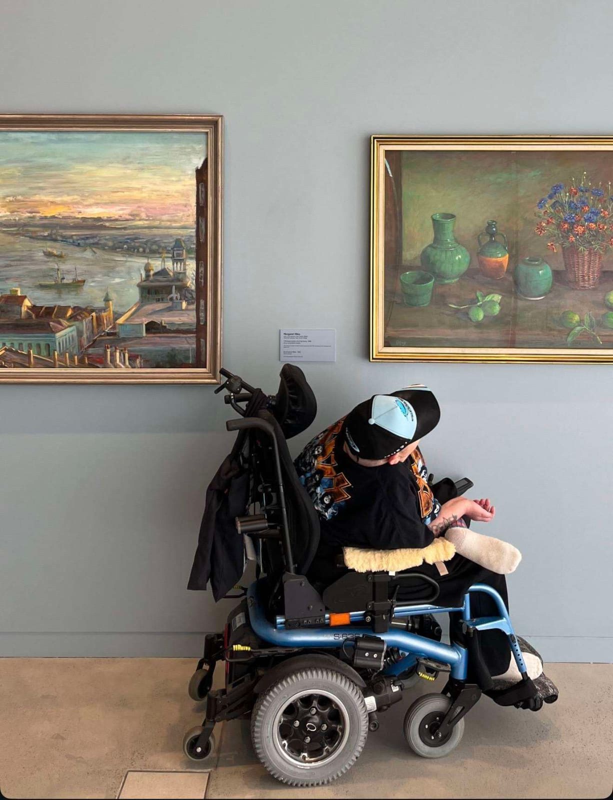A Pal Supports participant in a power wheelchair looking at paintings in a Newcastle gallery