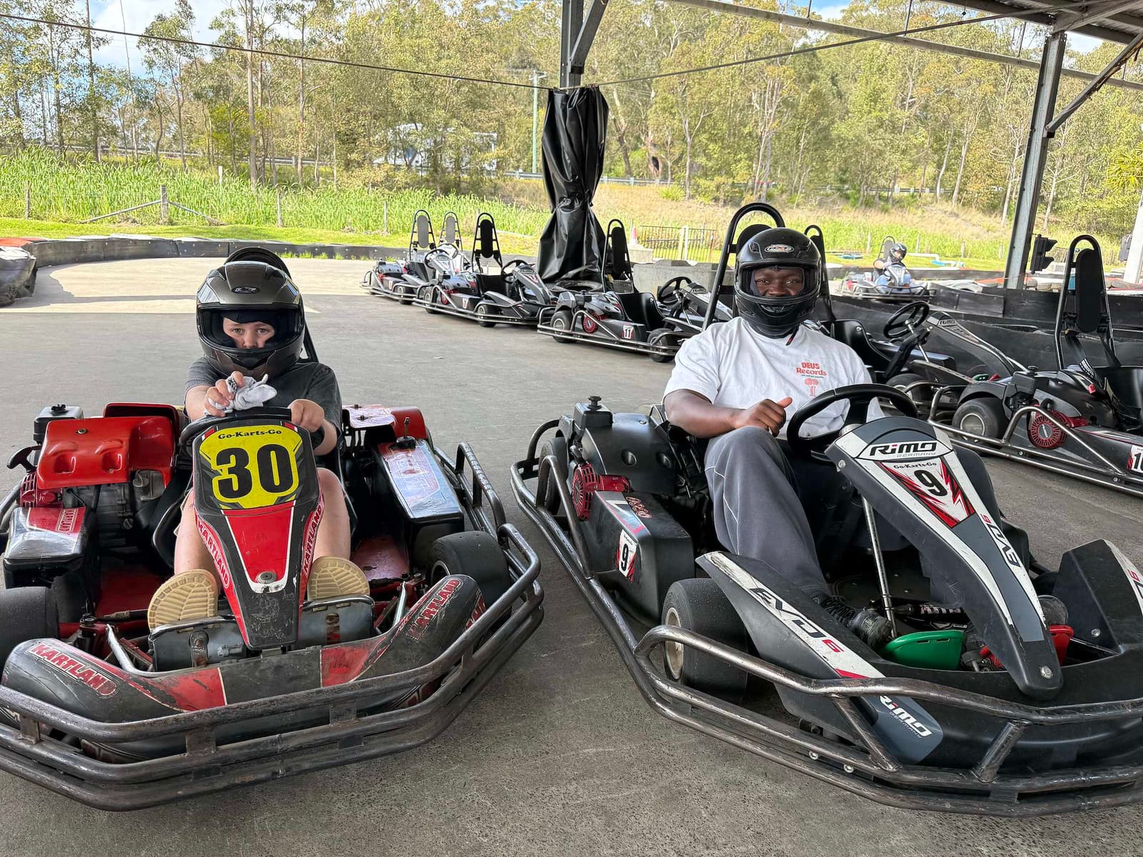 A Pal Supports participant and his worker lined up side by side in go karts, helmets on, ready to race